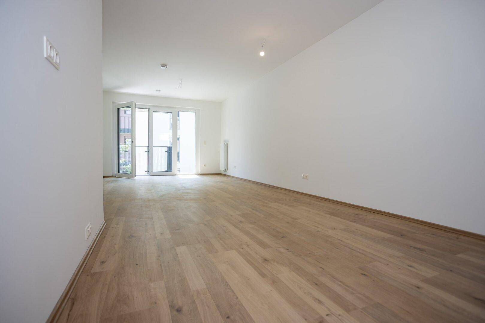 Heller, leerer Raum mit modernem Laminatboden und Zugang zu einem Balkon, ideal für individuelle Gestaltung.