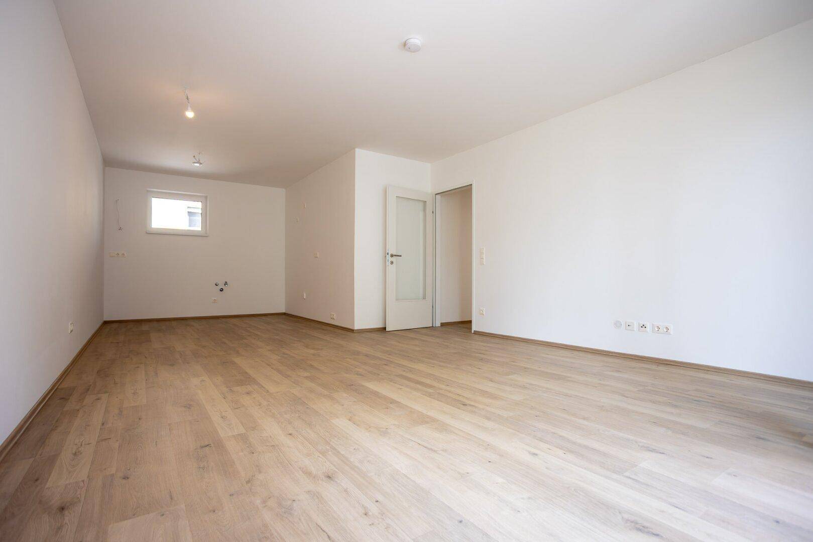 Geräumiger, leerer Raum mit hellem Laminatboden und weißen Wänden, bereit zur individuellen Gestaltung.