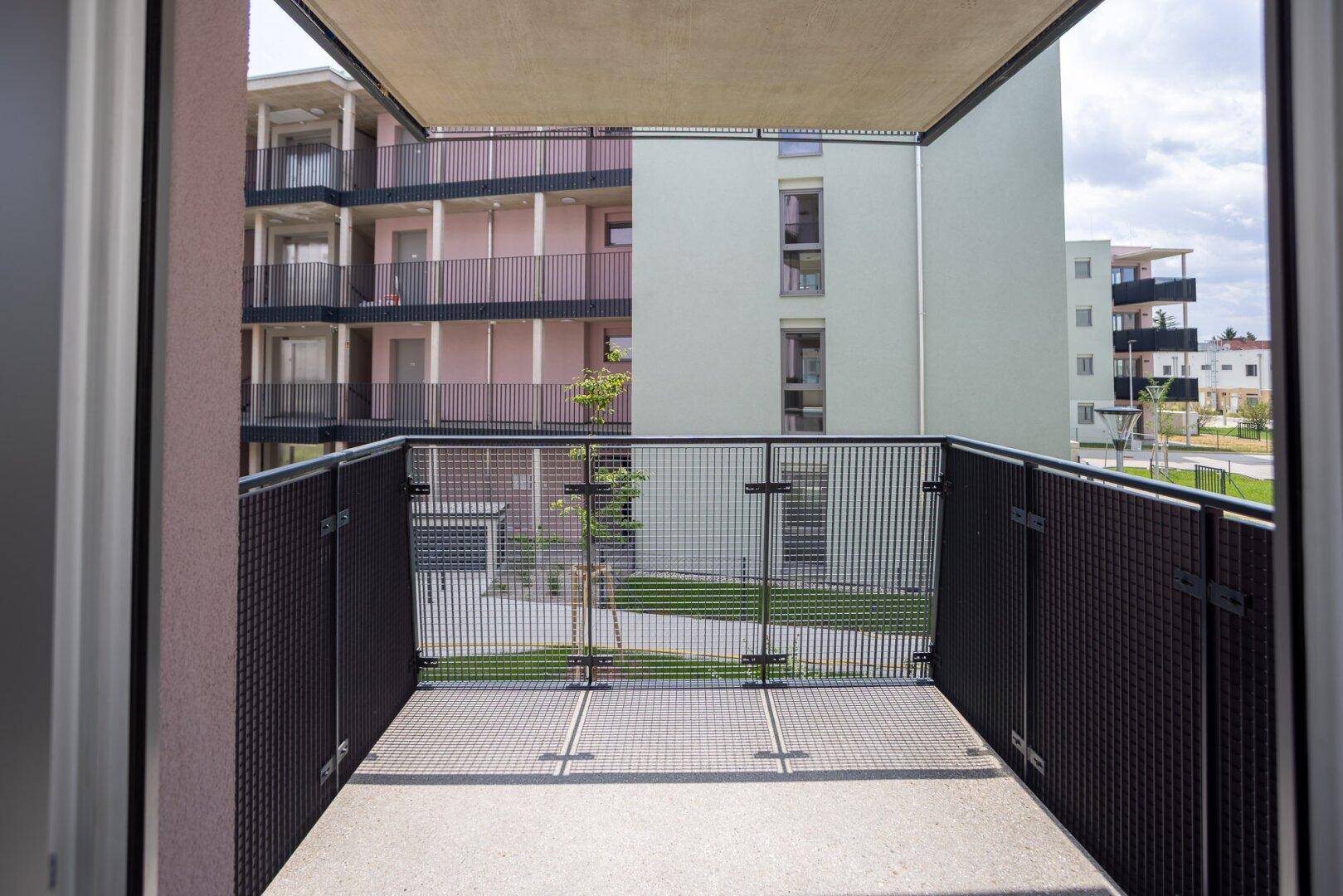 Balkon mit Gittergeländer und Ausblick auf die umliegenden Gebäude und die grüne Umgebung.