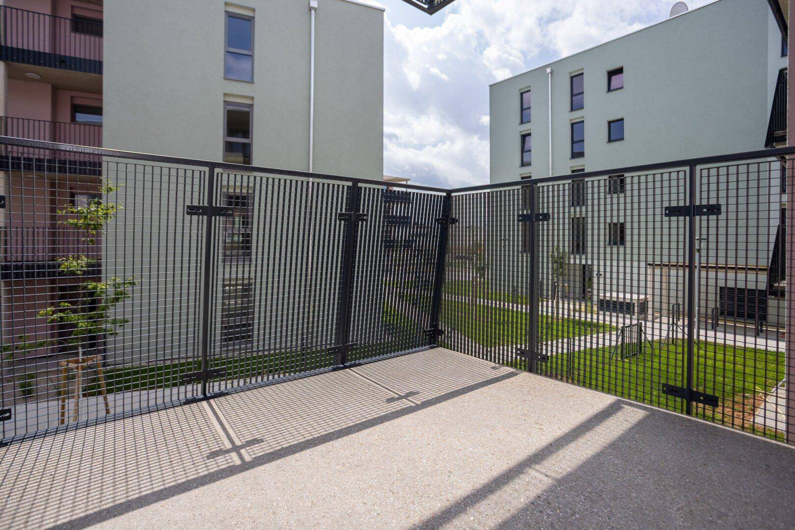Eckbalkon mit Gittergeländer und weitem Blick über den begrünten Innenhof der Wohnanlage.