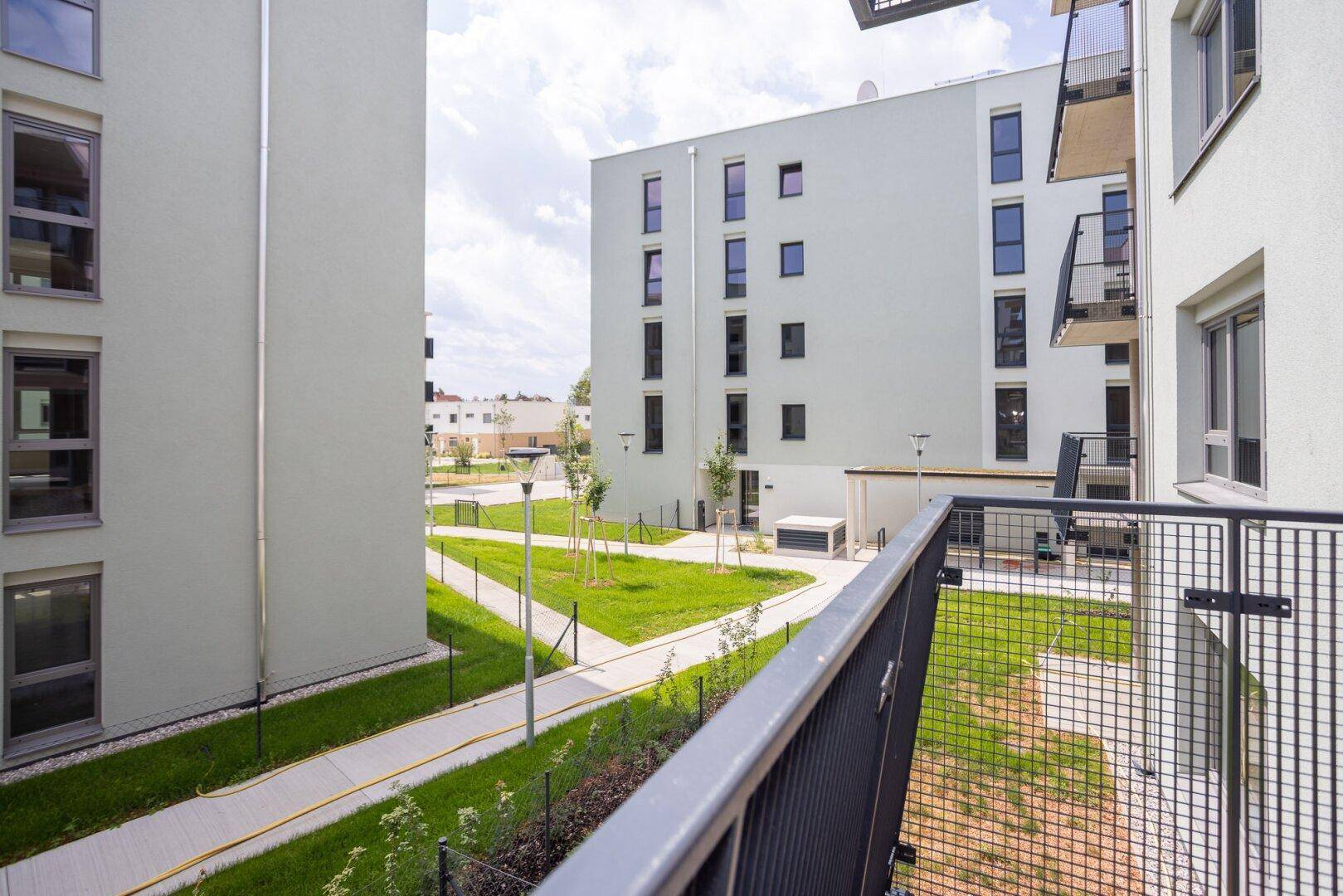 Blick von einem Balkon auf moderne Wohngebäude und die gepflegten Grünflächen der Anlage.