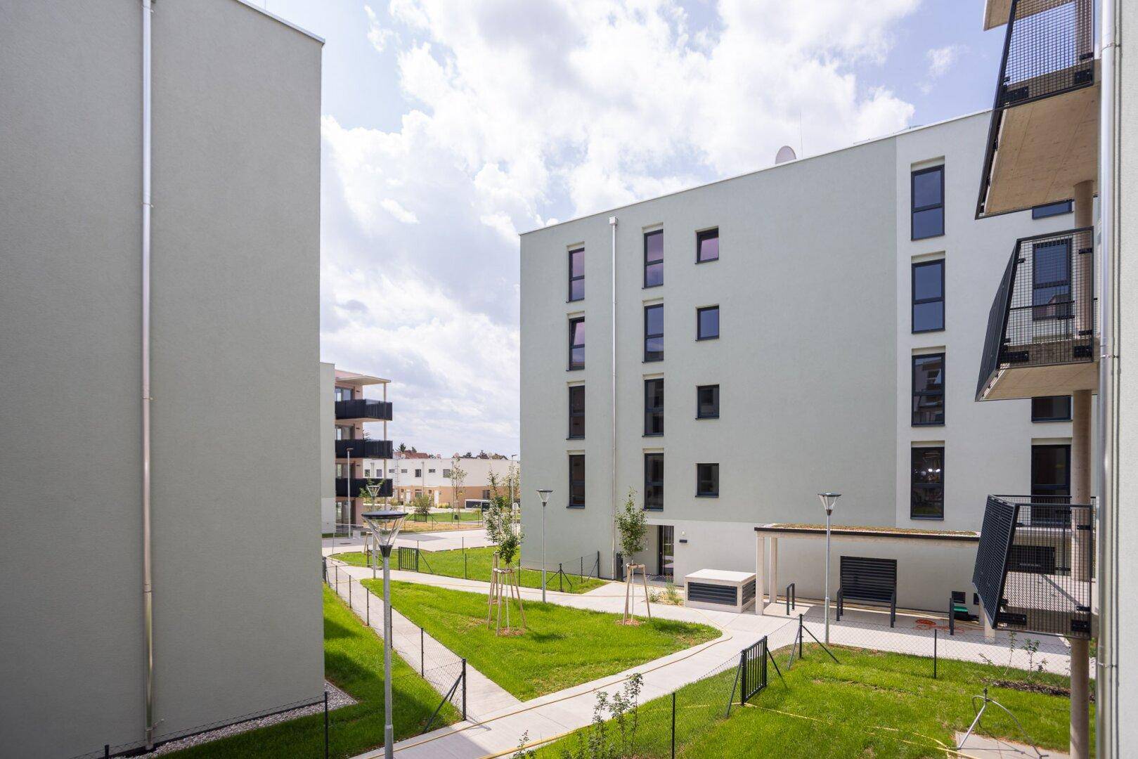 Moderne Wohngebäude mit hellen Fassaden, großen Fenstern und gepflegten Grünflächen im Außenbereich.