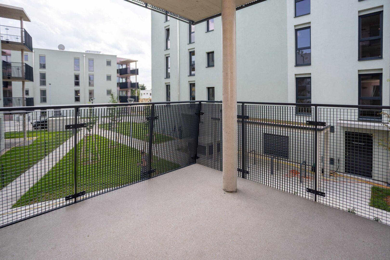 Geräumiger Balkon mit Gittergeländer und Blick auf die grüne Wohnanlage.