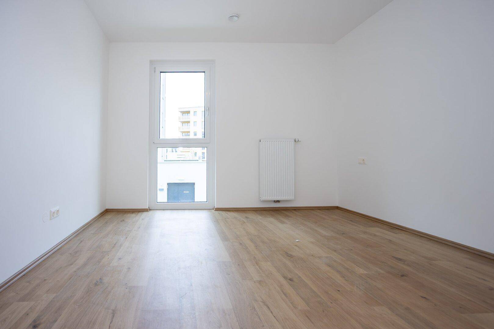 Leeres Schlafzimmer mit hellem Laminatboden, weißen Wänden und einem Fenster.