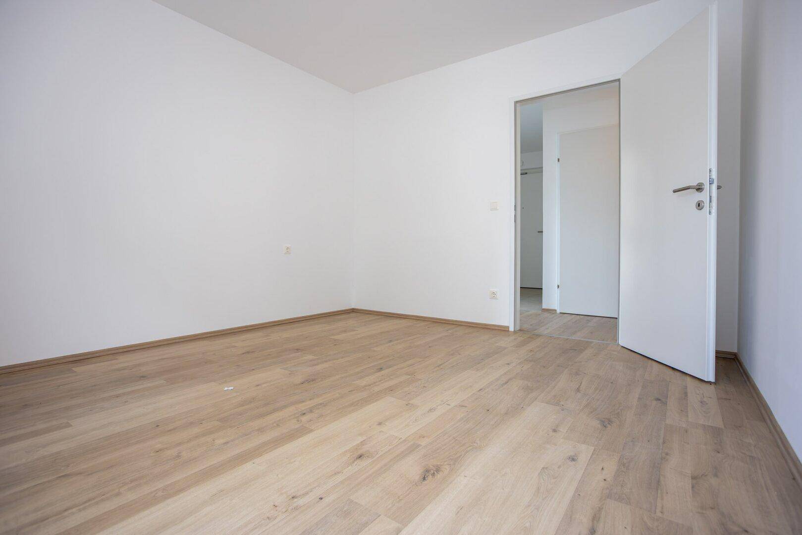 Leeres Zimmer mit Laminatboden und weiß gestrichenen Wänden, bereit zum Einzug.