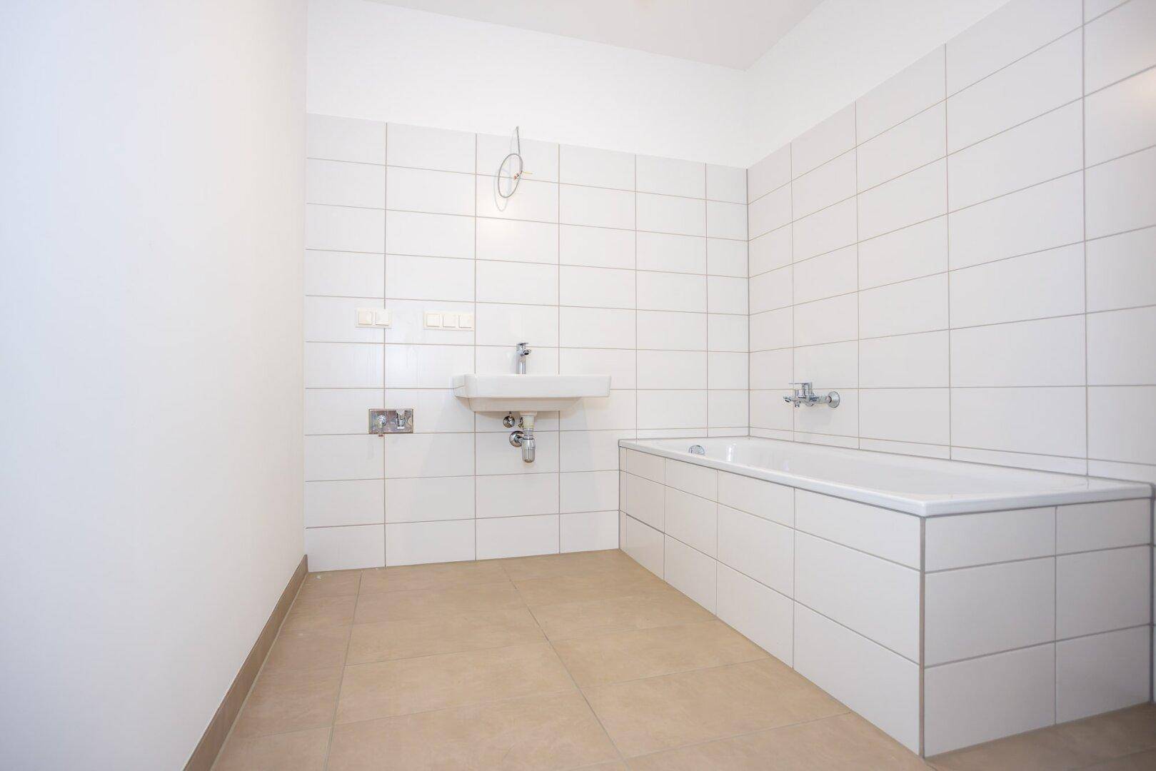 Helles Badezimmer mit Badewanne, Waschbecken und weißen Wandfliesen.
