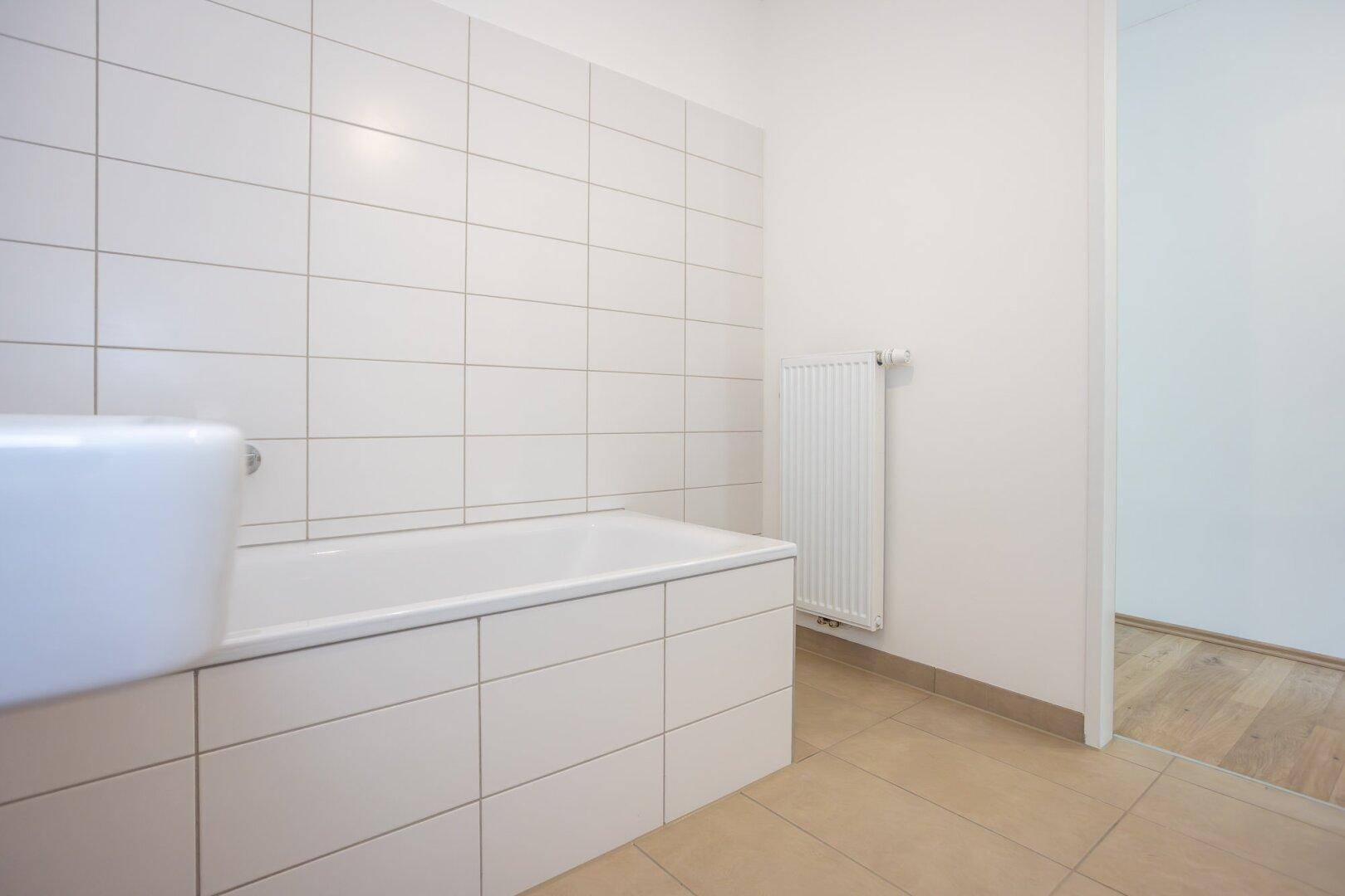 Modernes Badezimmer mit Badewanne, weißen Fliesen und Heizkörper, bereit zur Fertigstellung.