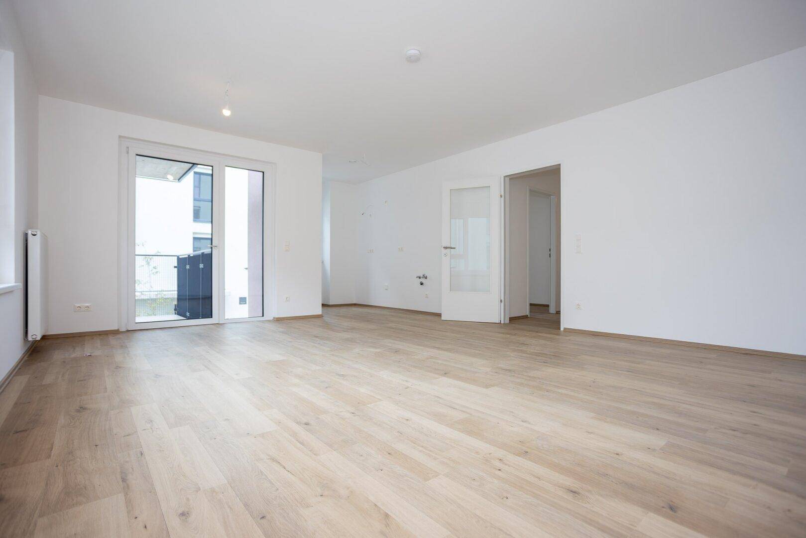 Geräumiges, helles Wohnzimmer mit Laminatboden und Schiebetür zum Balkon.