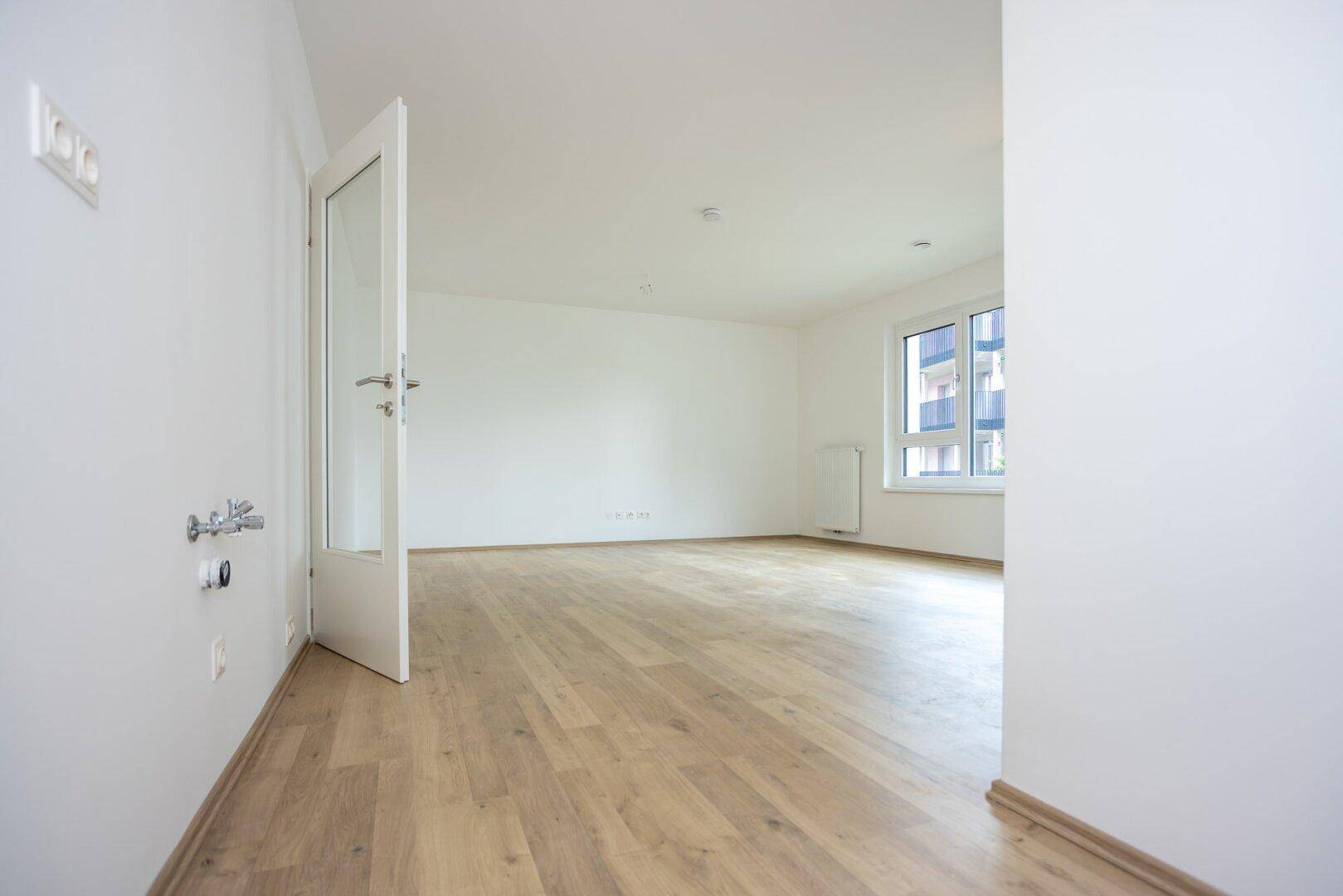 Leerer Küchenbereich mit Anschlüssen für Spüle und Geräte, bereit für die Installation.