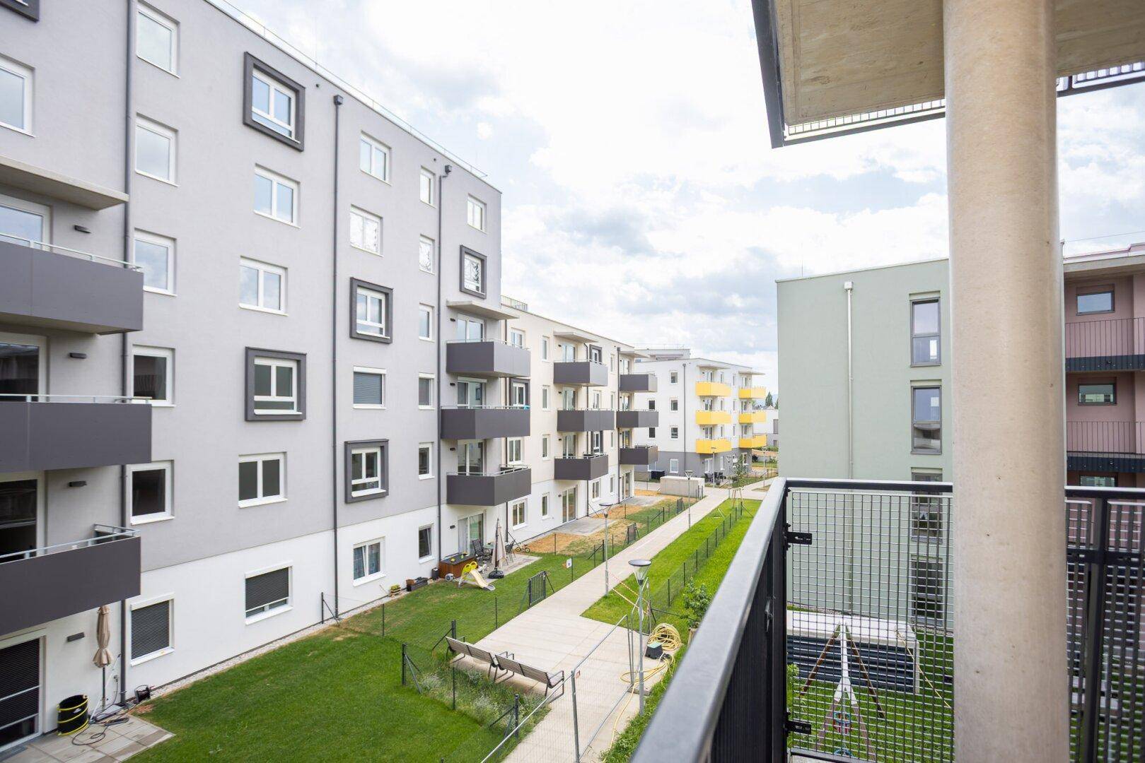 Blick vom Balkon auf den begrünten Innenhof mit Spielplatz und modernen Wohngebäuden.