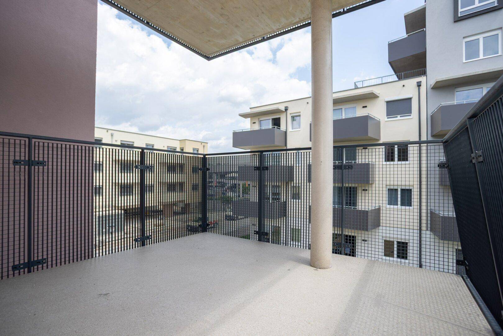 Geräumiger Balkon mit Betonboden und Metallgeländer, umgeben von modernen Wohngebäuden.