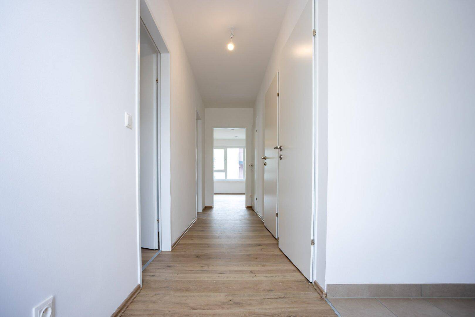 Heller Flur mit Laminatboden und weißen Wänden, der zu den verschiedenen Zimmern führt.