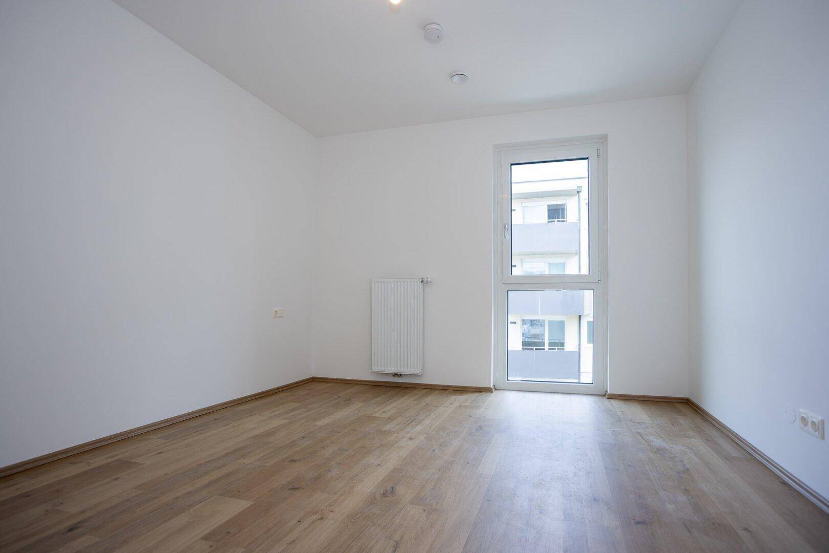Freundliches Schlafzimmer mit hellem Laminatboden und einem großen Fenster für viel Tageslicht.