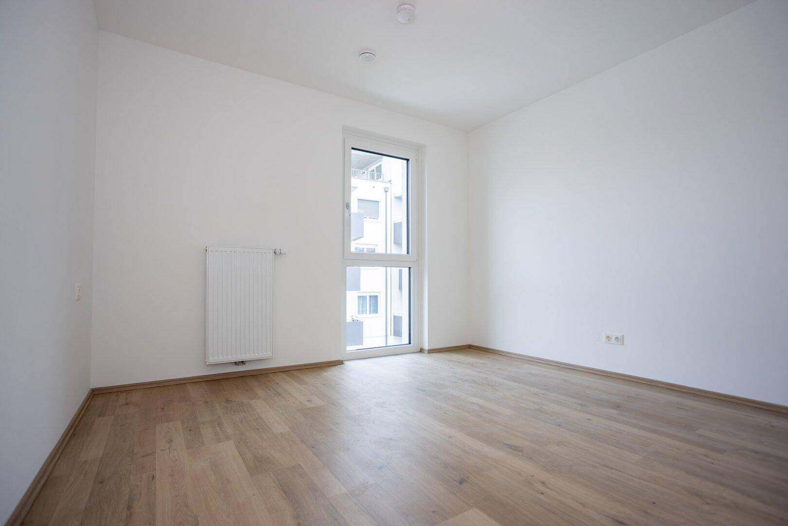 Geräumiges Schlafzimmer mit hellem Laminatboden und viel Tageslicht durch das große Fenster.