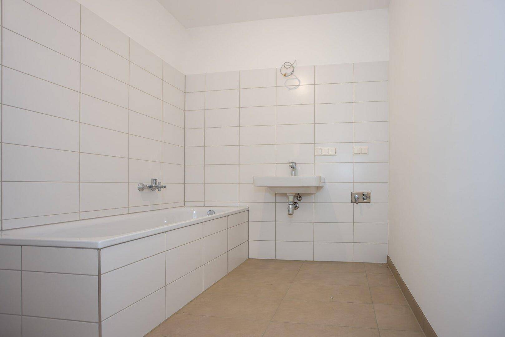 Modernes Badezimmer mit weißen Fliesen, Badewanne und Waschbecken.