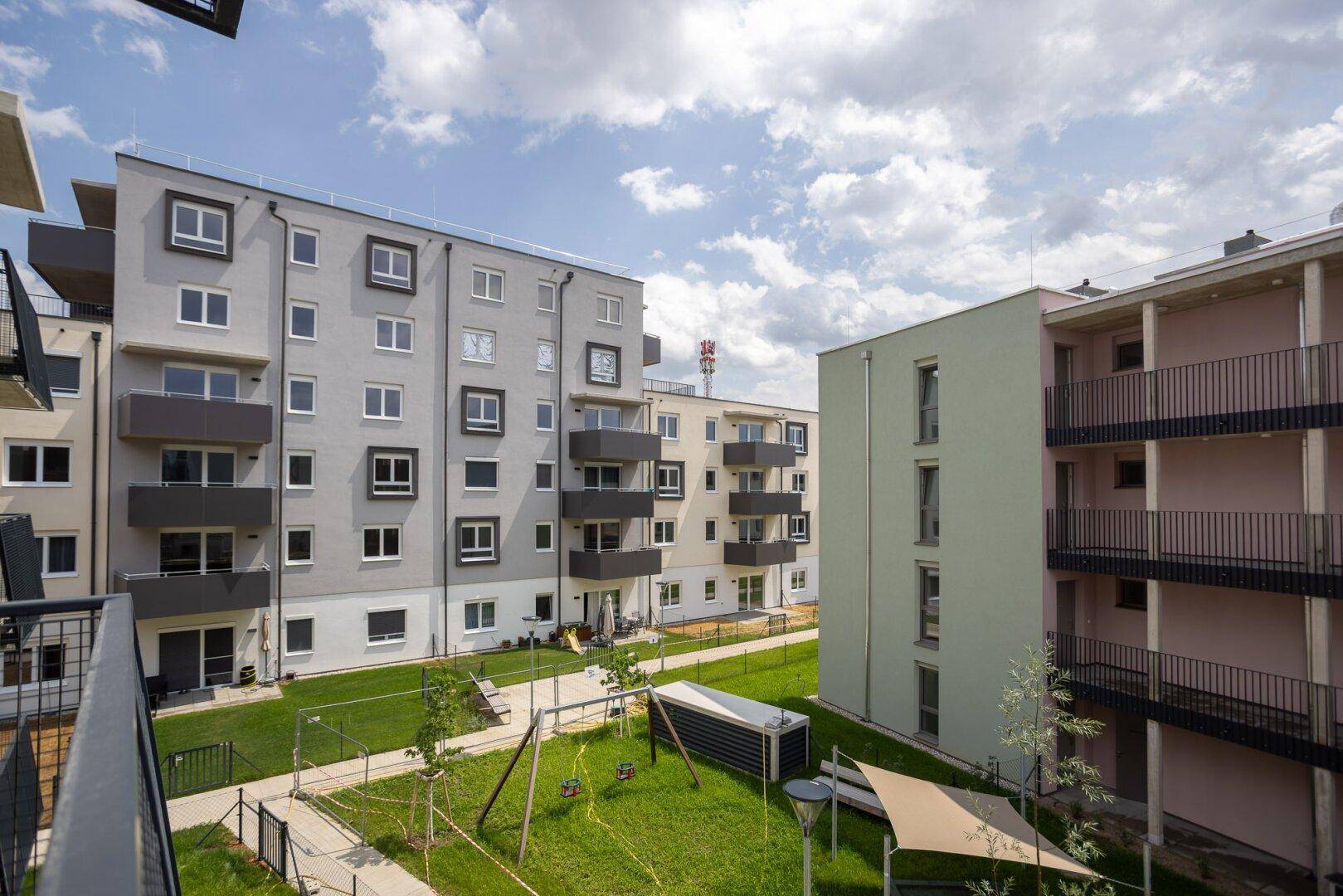 Moderne Wohngebäude mit Balkonen und einem Gemeinschaftsspielplatz im grünen Innenhof.