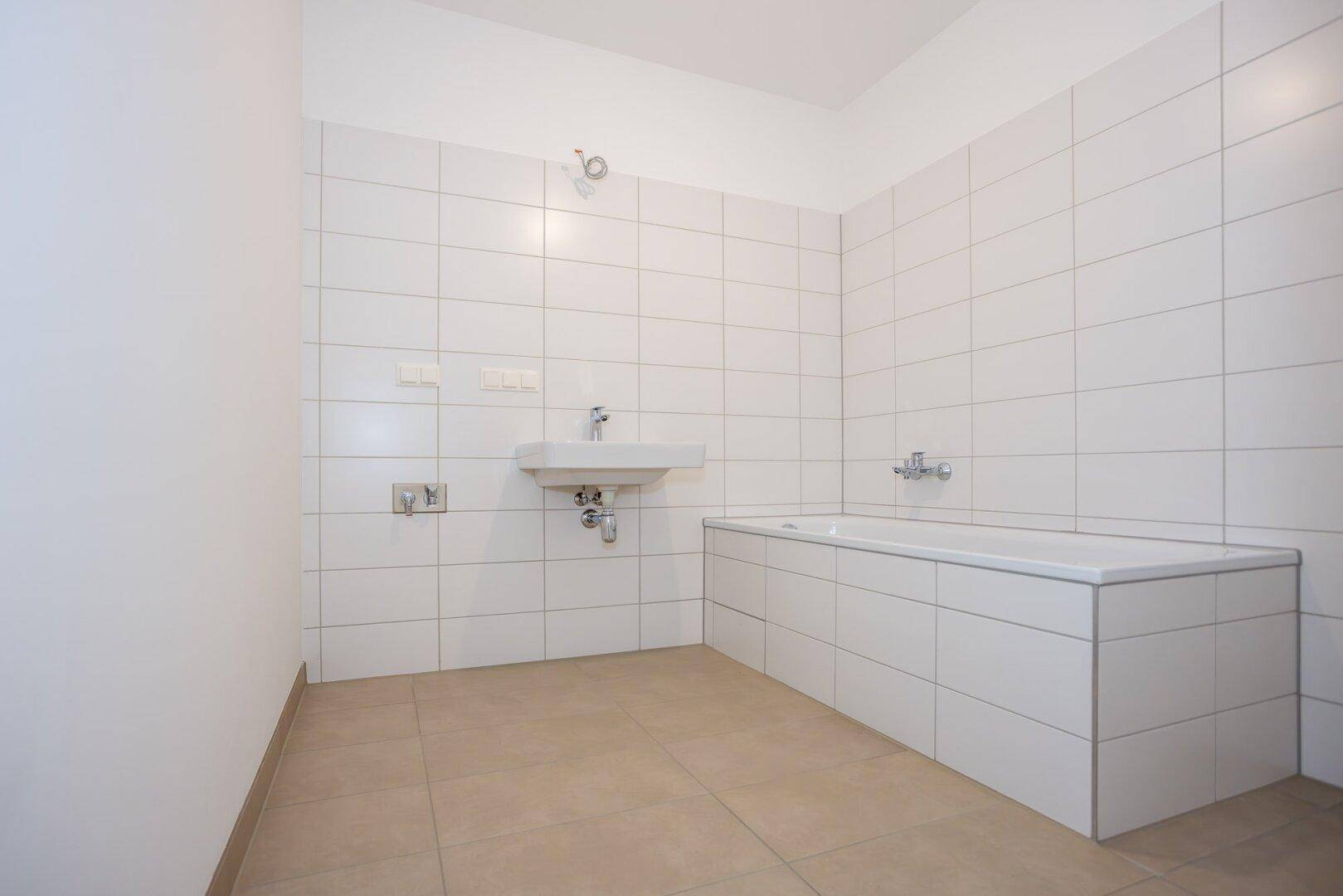 Modernes Badezimmer mit weißen Fliesen, Badewanne und Waschbecken.
