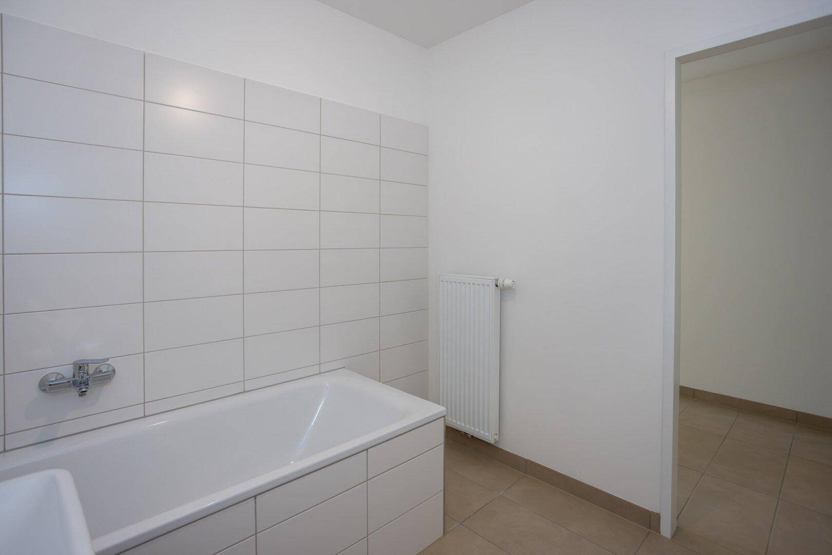 Badezimmer mit weißen Wandfliesen, Badewanne und Heizkörper.