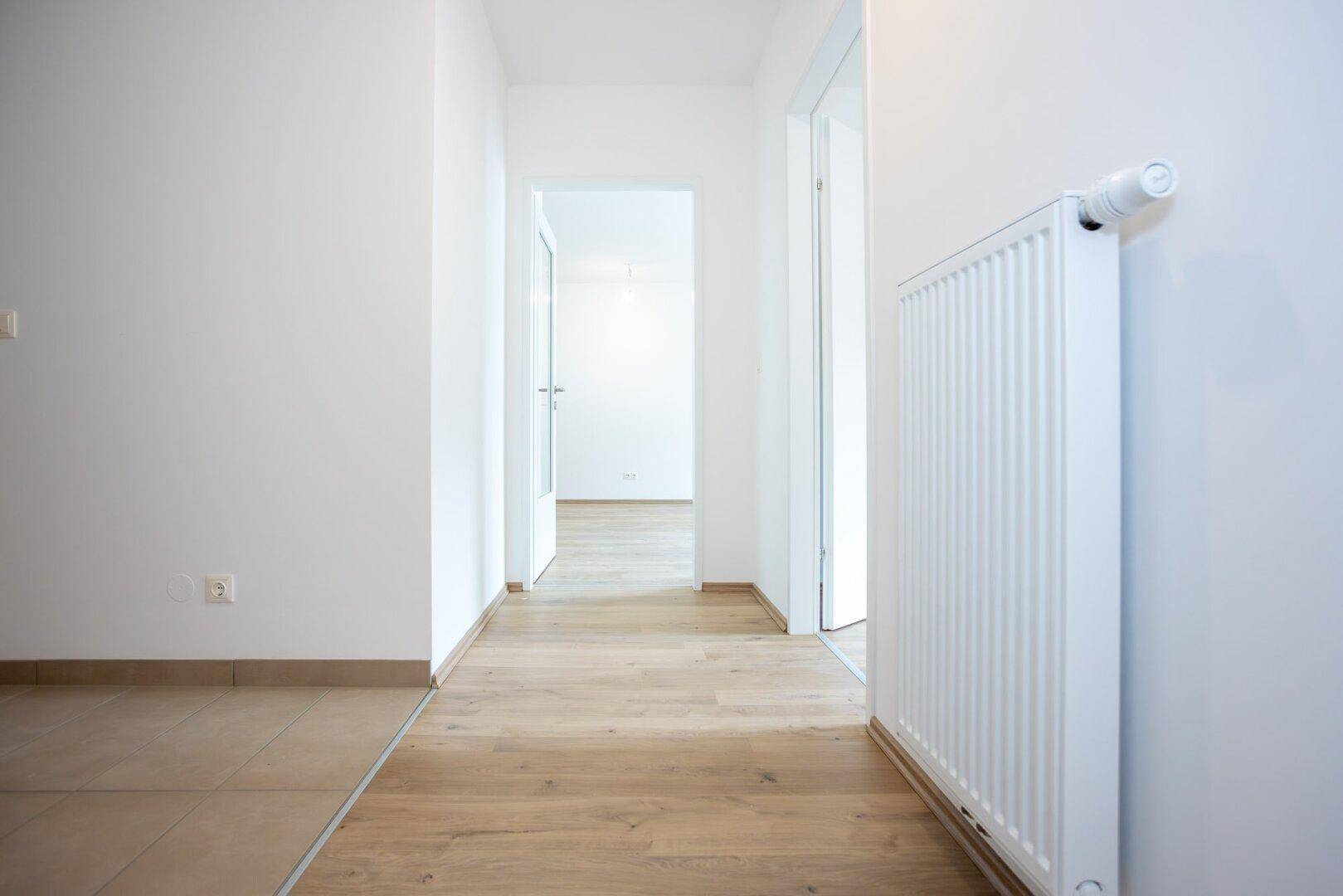 Heller Flur mit Laminatboden und Übergang zu einem gefliesten Bereich.