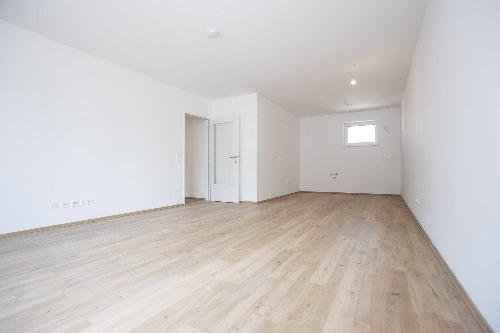 Heller, leerer Raum mit Laminatboden und einem kleinen Fenster.