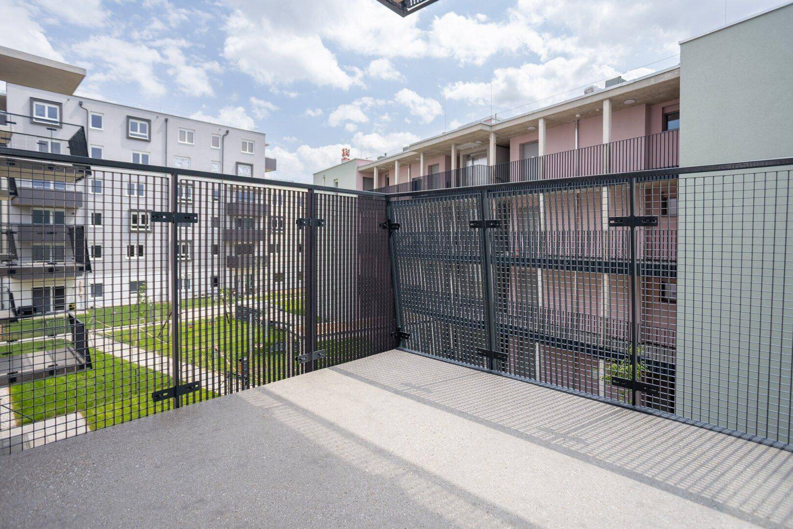 Balkon mit Metallgeländer und Blick auf den begrünten Innenhof des Wohnkomplexes.
