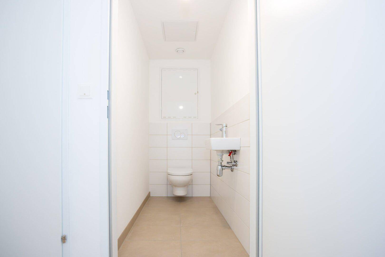 Modernes Gäste-WC mit wandhängender Toilette, kleinem Waschbecken und hellen Fliesen.