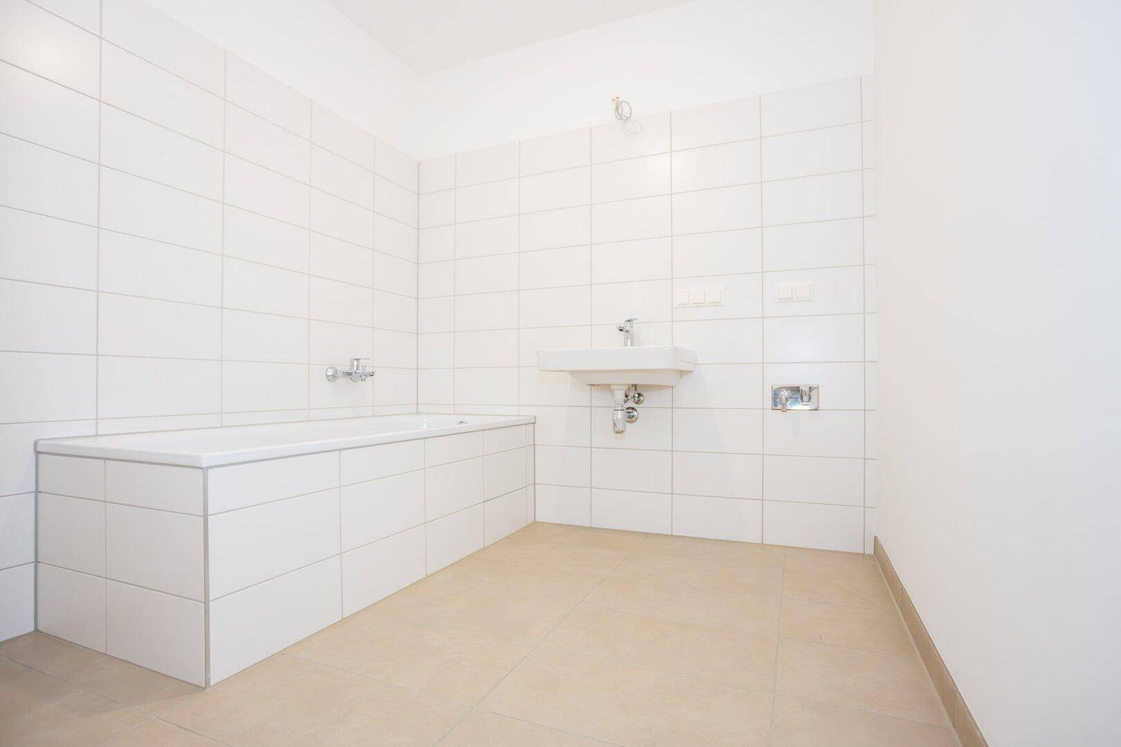 Helles Badezimmer mit Badewanne, Waschbecken und weißen Fliesen an Wänden und Boden.