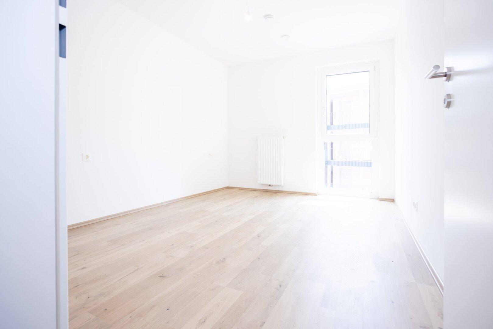 Leeres Schlafzimmer mit hellem Holzboden und einem großen Fenster für viel Tageslicht.