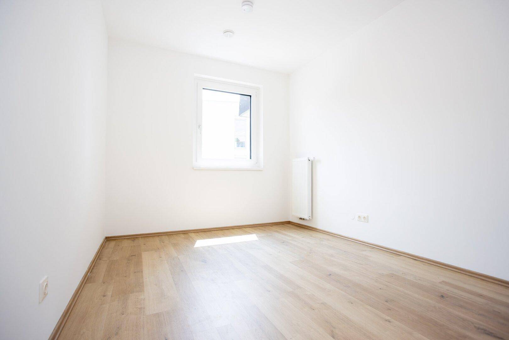 Unmöbliertes Zimmer mit hellem Holzboden und einem Fenster, ideal als Schlaf- oder Arbeitszimmer.
