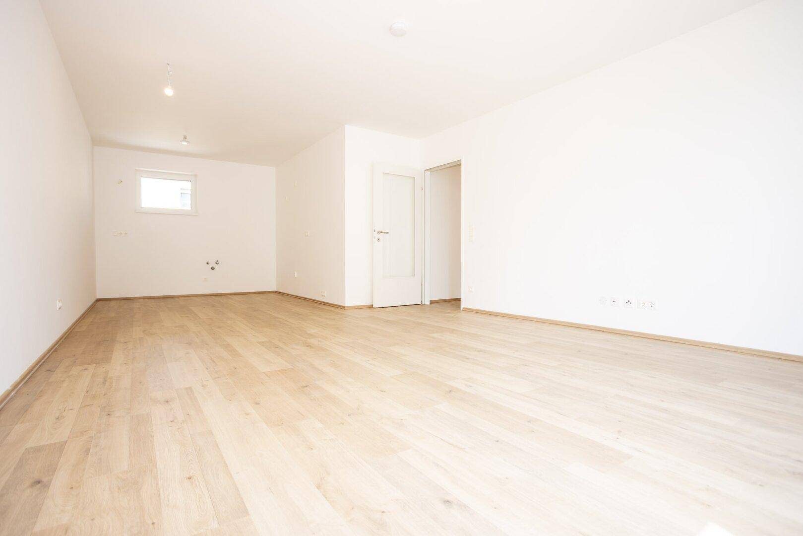 Großer, heller Raum mit Holzboden und einem kleinen Fenster, vielseitig nutzbar.