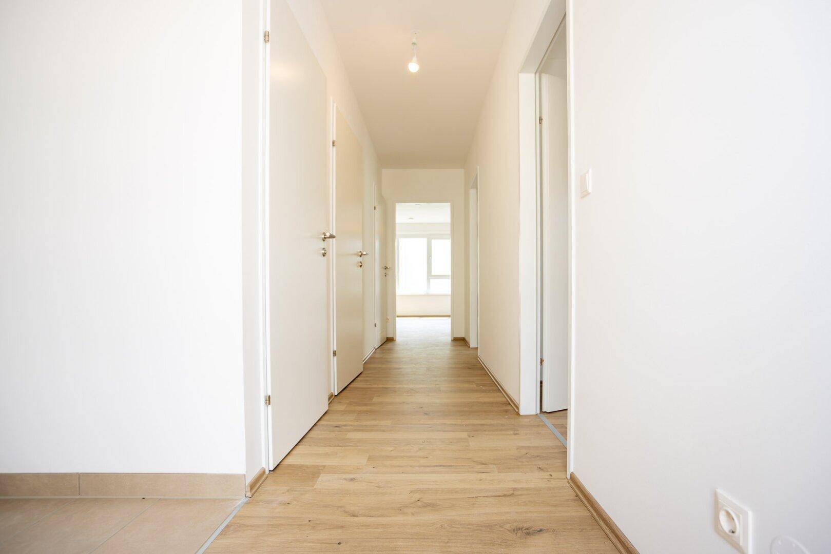 Heller Flur mit hellem Laminatboden und weißen Türen in einem modernen Neubau.
