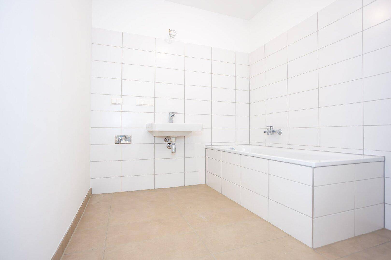 Modernes Badezimmer mit weißen Fliesen, einer Badewanne und einem Wandwaschbecken.