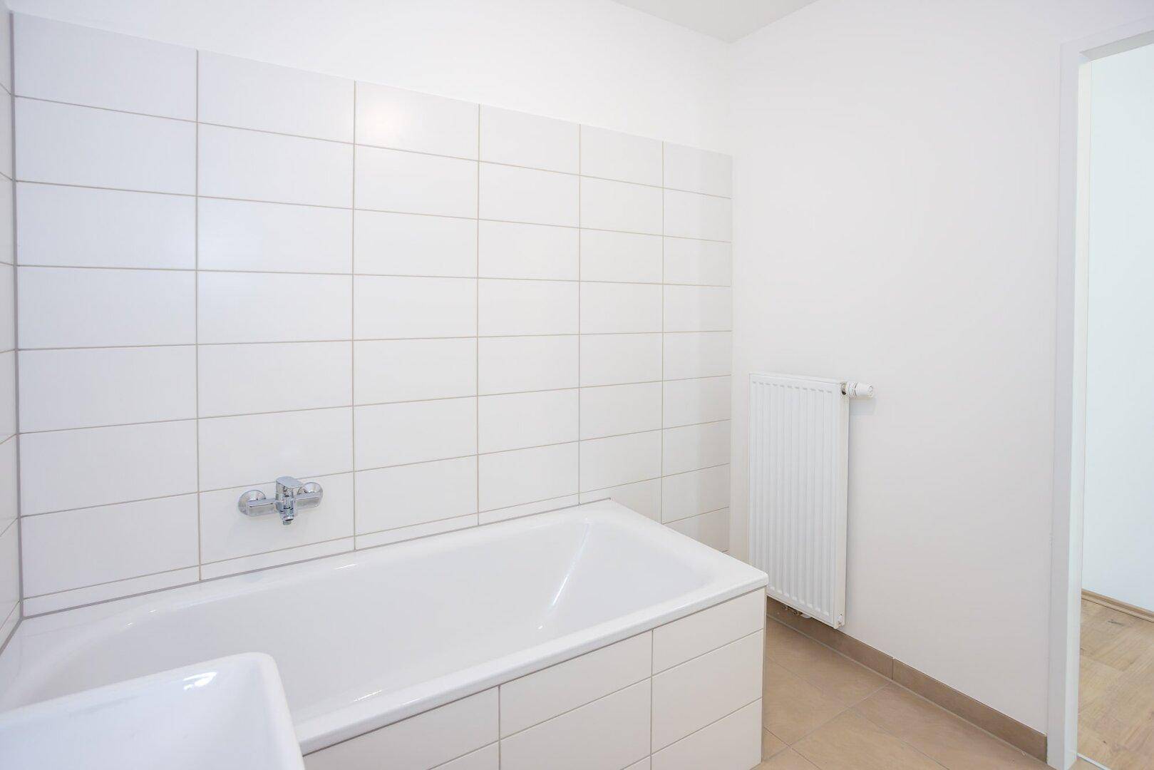 Helles Badezimmer mit weißen Wandfliesen und einer Badewanne in einem Neubau.