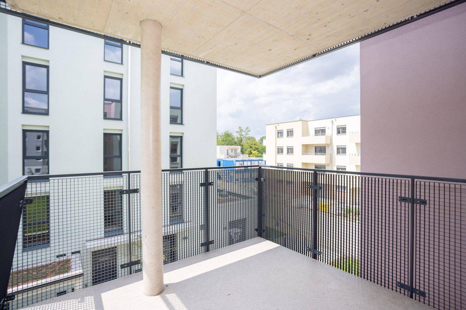 Heller Balkon mit Gittergeländer und Blick auf die moderne Wohnanlage.