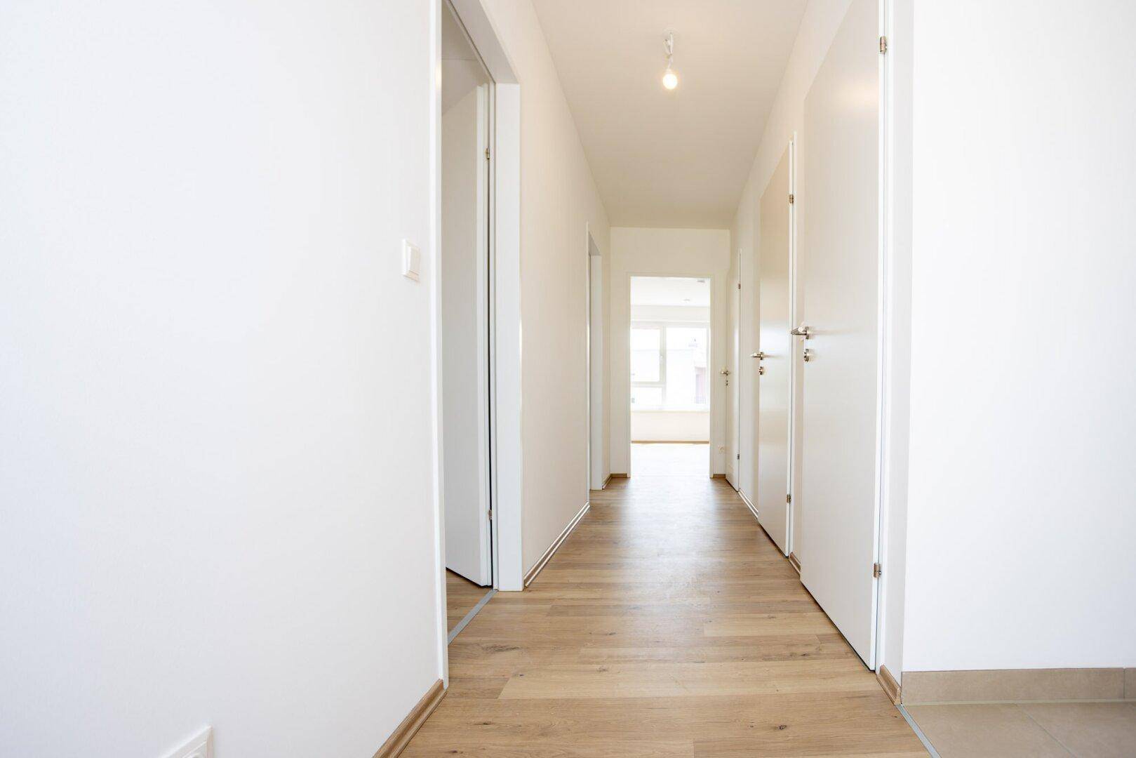 Heller Flur mit Laminatboden und weißen Türen, der zu verschiedenen Räumen führt.