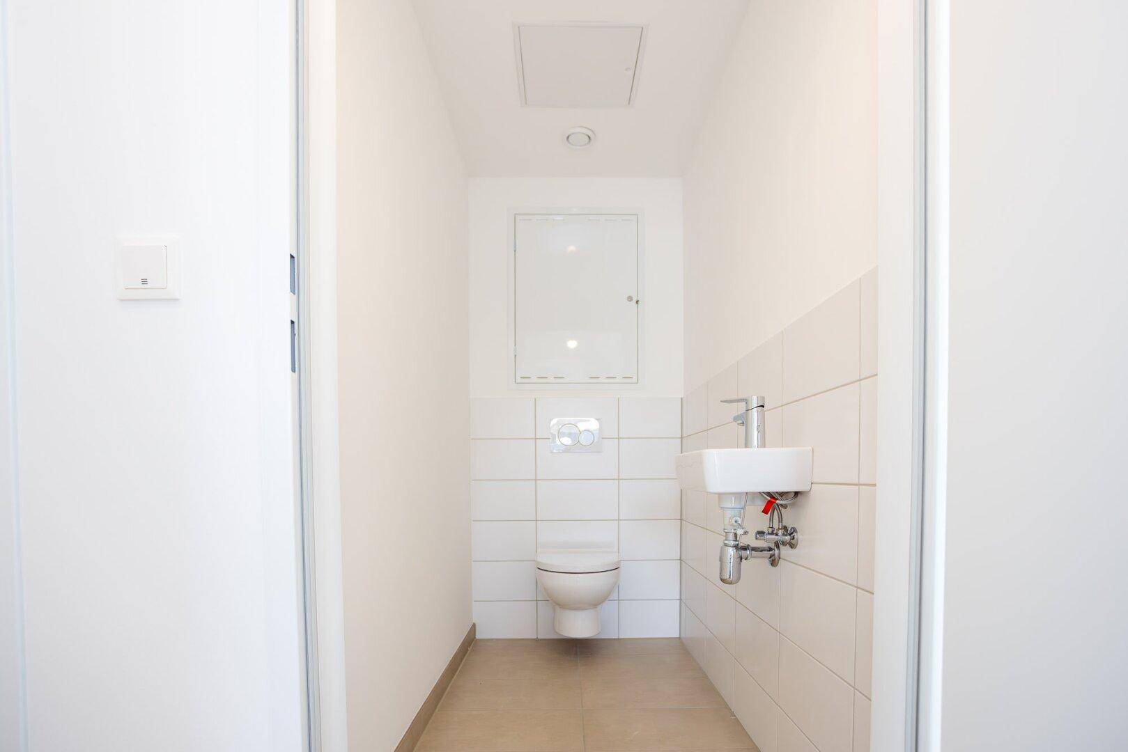 Kleines Gäste-WC mit weißen Fliesen, Toilette und Handwaschbecken, funktional und hell.