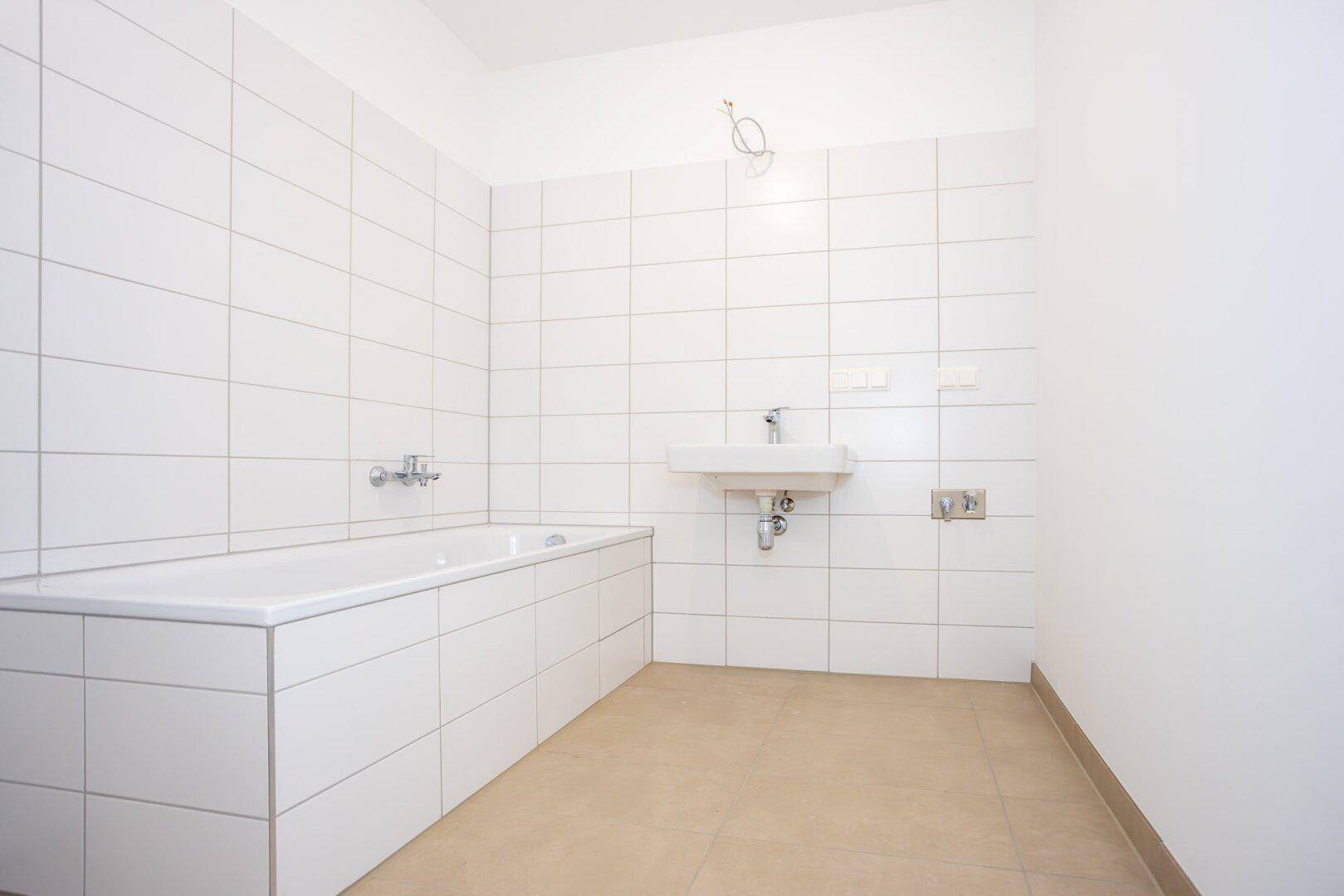 Modernes Badezimmer mit weißen Wandfliesen, beigefarbenem Boden und einer Badewanne.