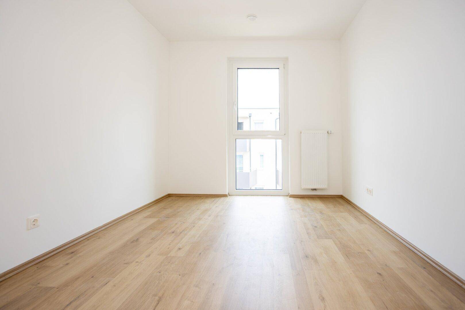 Lichtdurchflutetes Zimmer mit modernem Laminatboden und weiß gestrichenen Wänden, bereit zum Einzug.