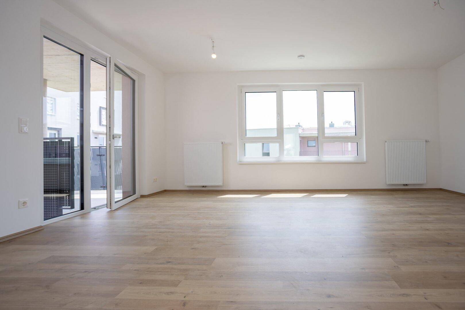 Heller Wohnbereich mit Laminatboden, großen Fenstern und direktem Zugang zum Außenbereich.