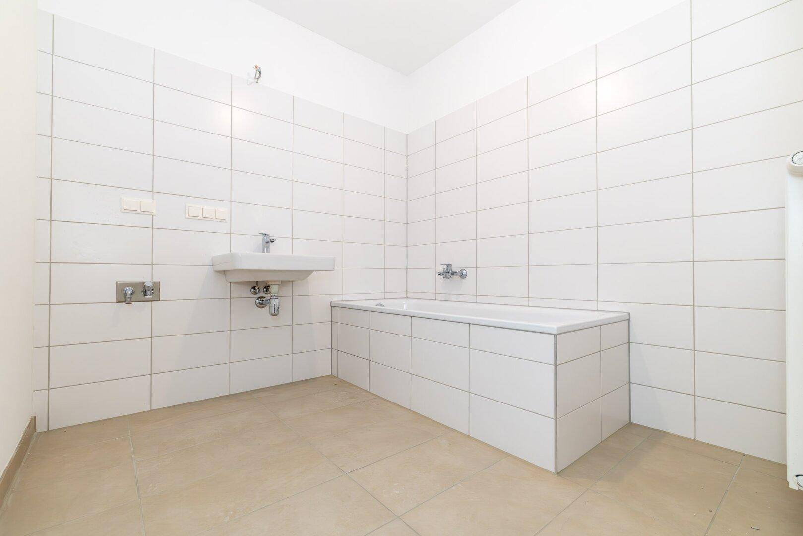 Helles Badezimmer mit Badewanne, Waschbecken und weißen Wandfliesen, funktional gestaltet.