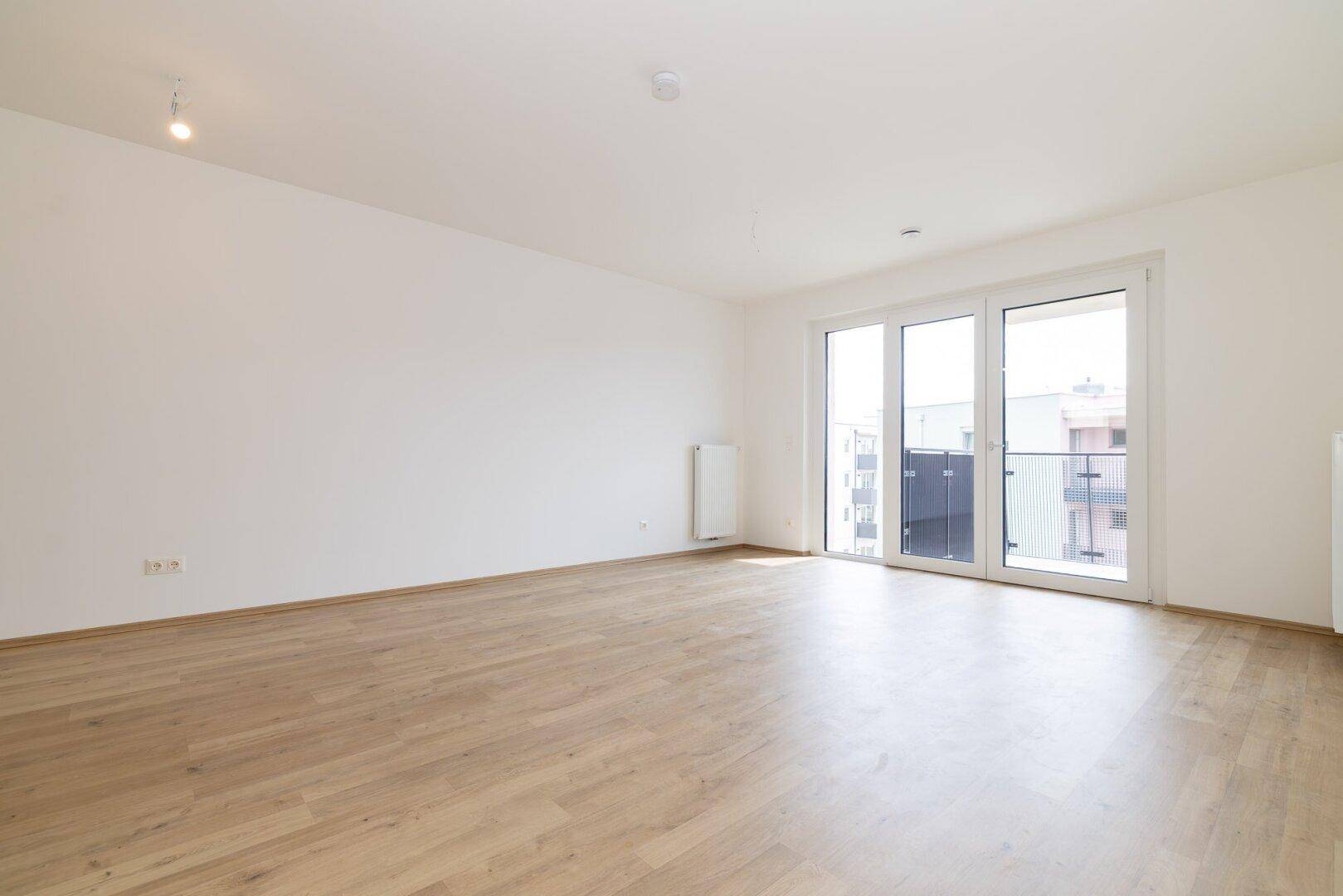 Großes, helles Wohnzimmer mit Laminatboden und Zugang zu einem Balkon, vielseitig nutzbar.