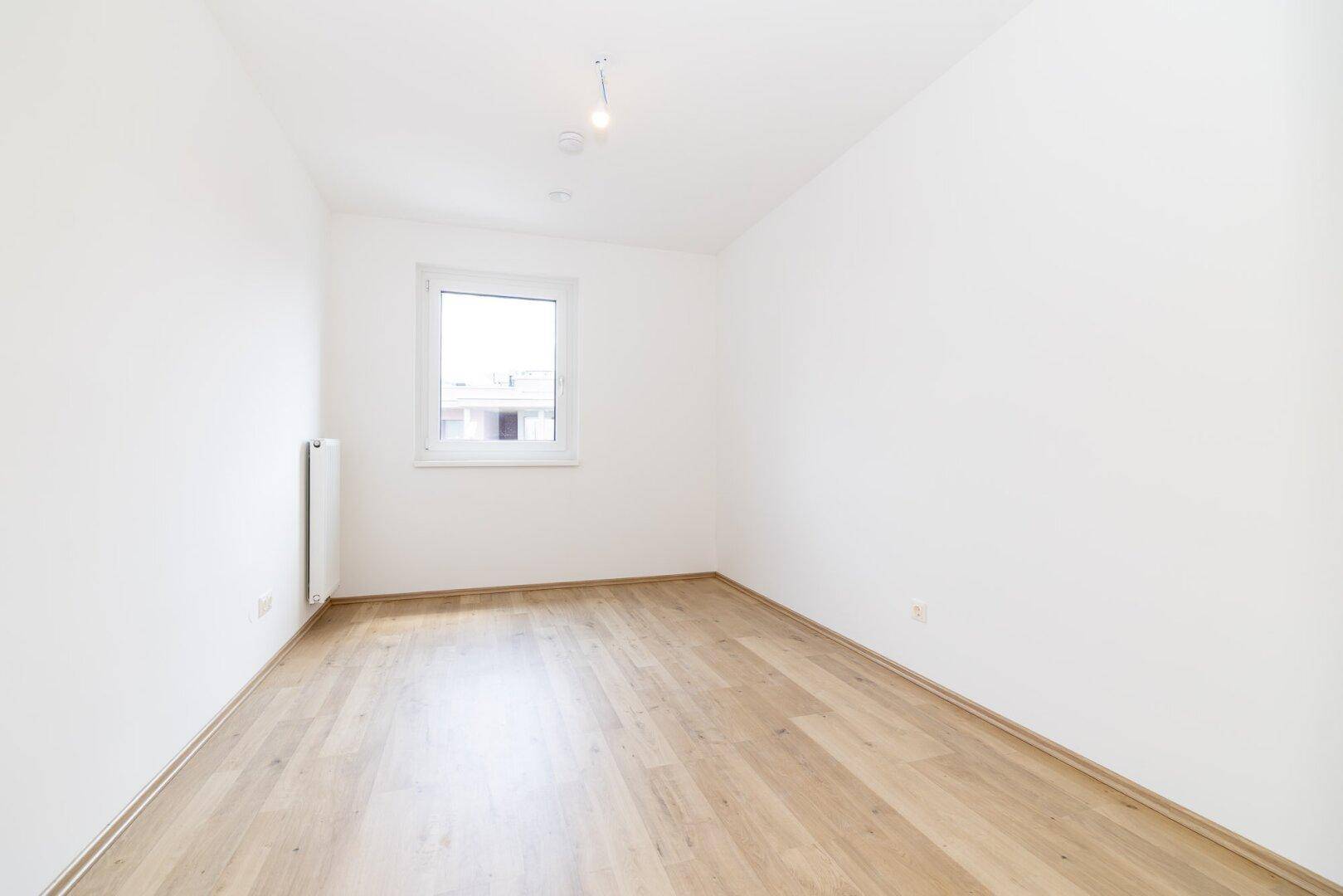 Ruhiges Schlafzimmer mit Laminatboden und einem Fenster, bereit für persönliche Einrichtung.