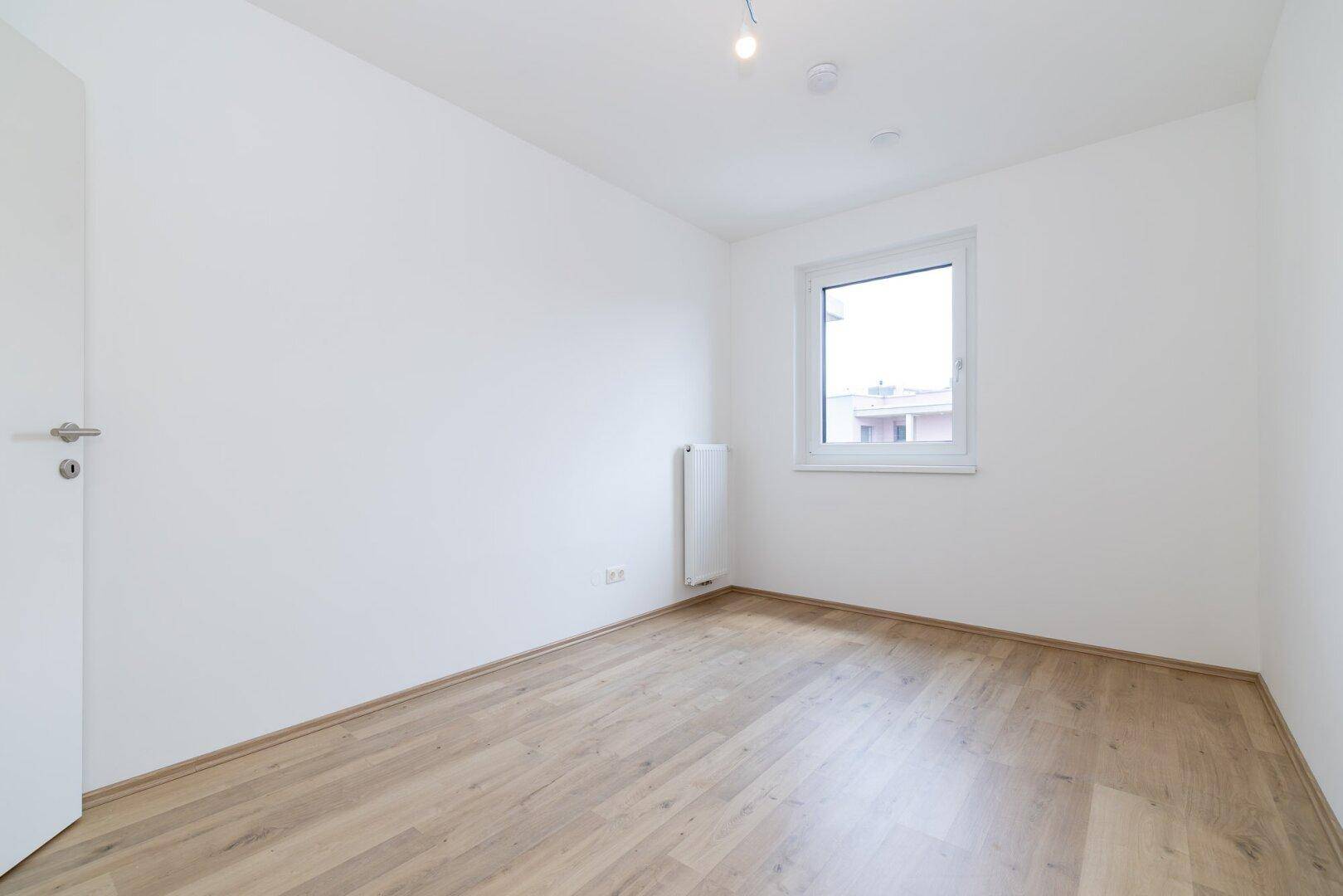 Helles Zimmer mit Laminatboden und einem Fenster, ideal als Schlaf- oder Arbeitszimmer.