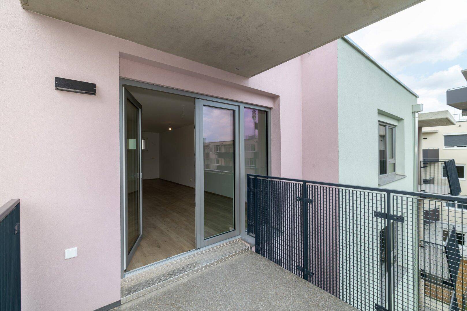 Balkon mit Blick auf die rosa Fassade des Gebäudes und offene Türen zum hellen Innenraum.