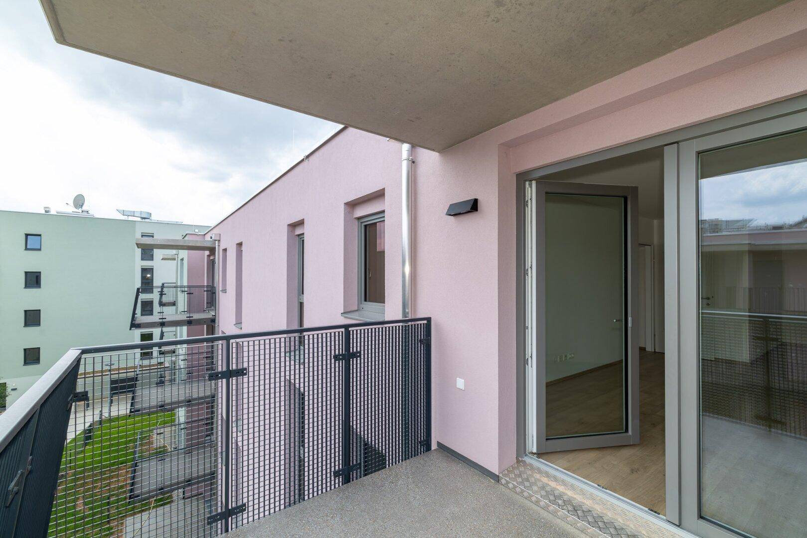 Balkon mit Blick auf die moderne Architektur der umliegenden Gebäude und eine rosa Fassade.