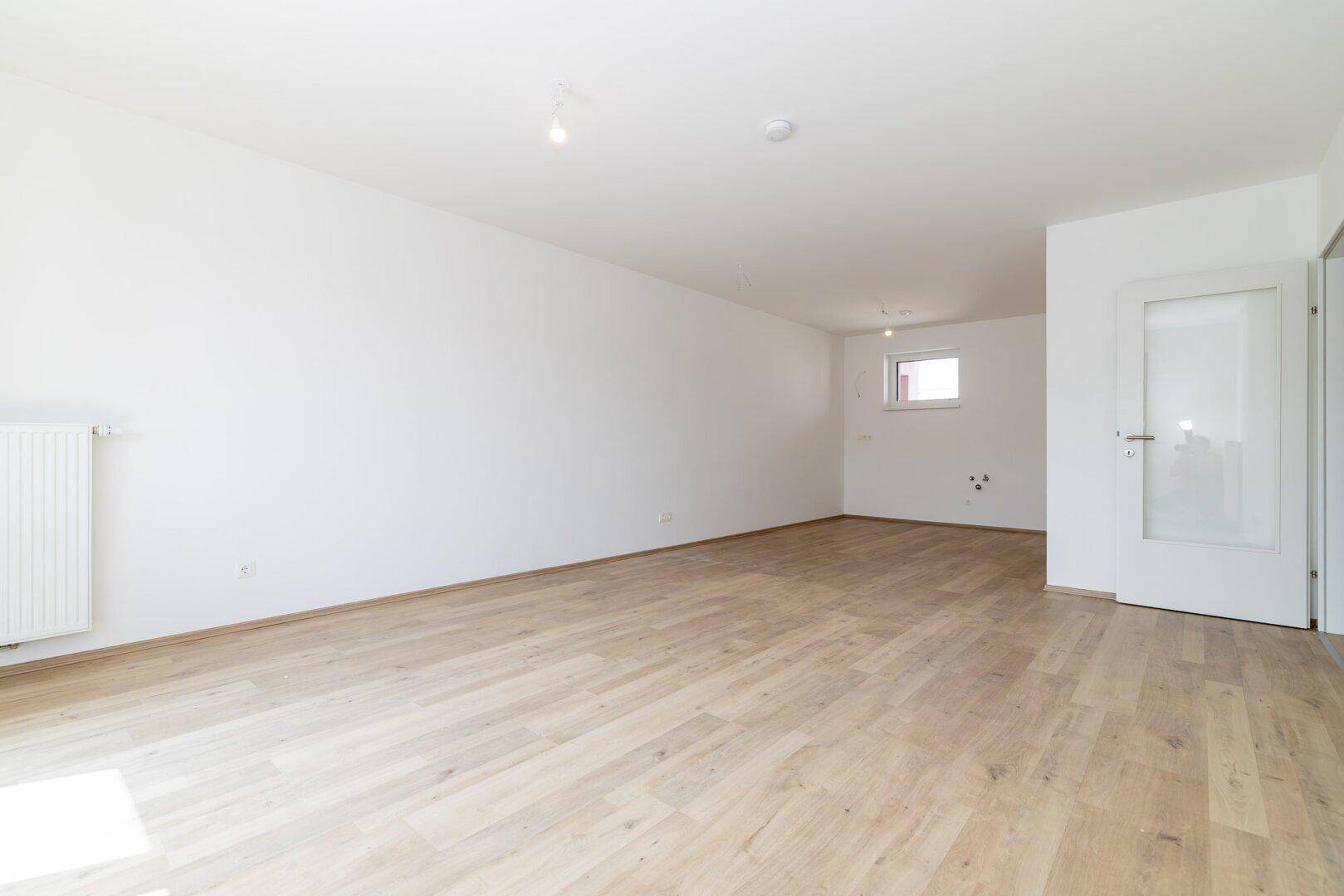 Heller und geräumiger Wohnbereich mit Laminatboden und weiß gestrichenen Wänden.