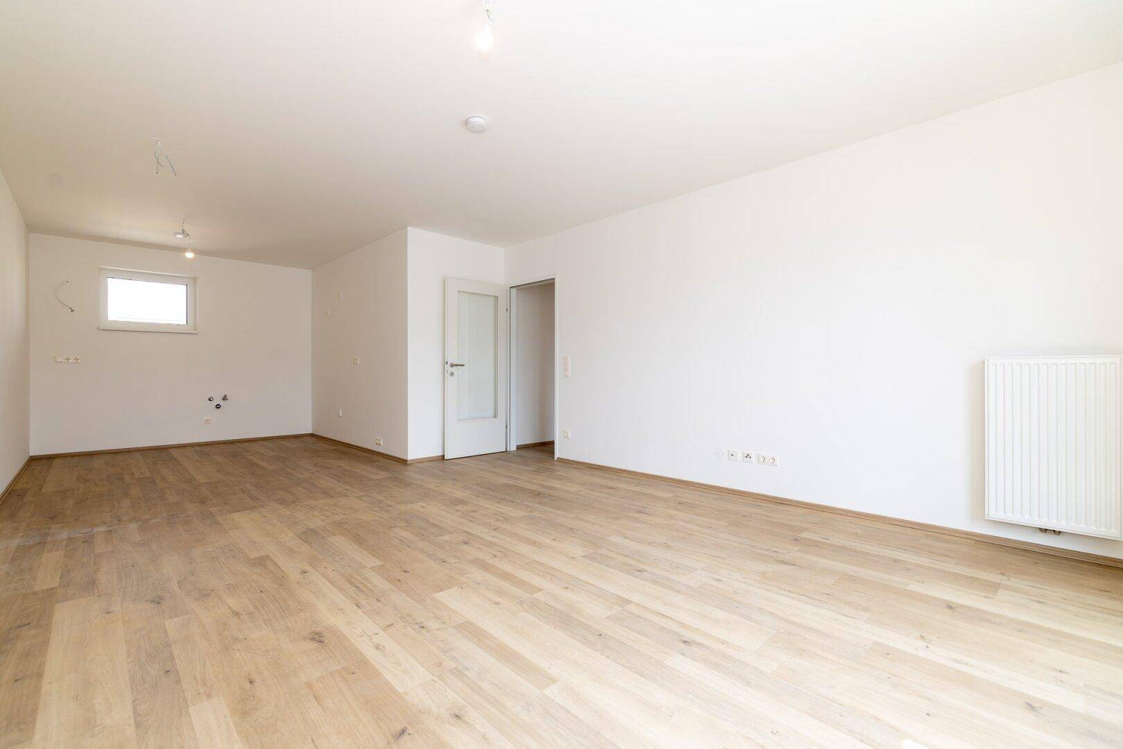 Geräumiger, heller Wohnbereich mit Laminatboden und weiß gestrichenen Wänden, bereit zur Einrichtung.