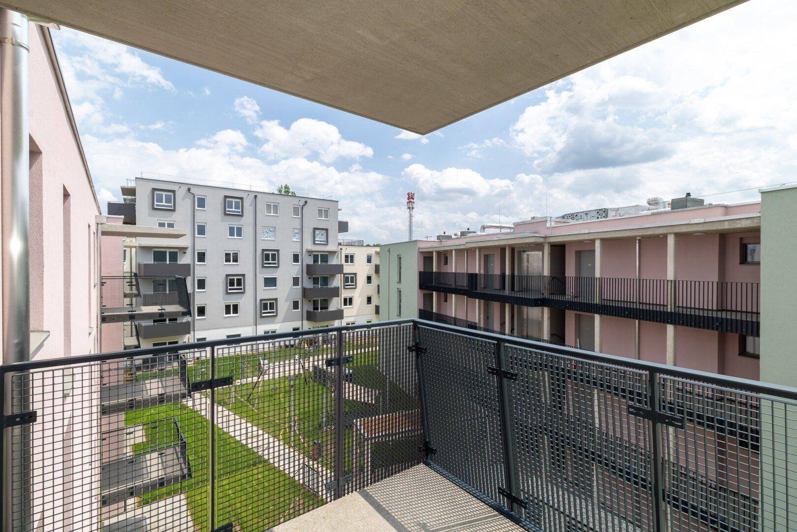 Weitläufiger Blick vom Balkon auf den grünen Innenhof und die moderne Wohnanlage unter blauem Himmel.