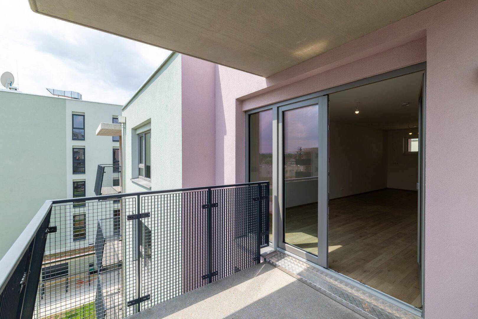 Balkon mit großer Glasschiebetür, die in einen hellen, leeren Wohnraum führt.