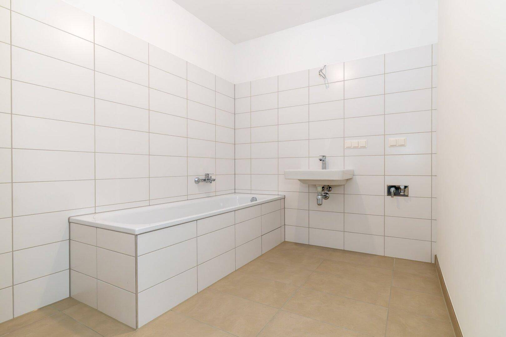Modern gefliestes Badezimmer mit Badewanne und Waschbecken, bereit zur Fertigstellung.